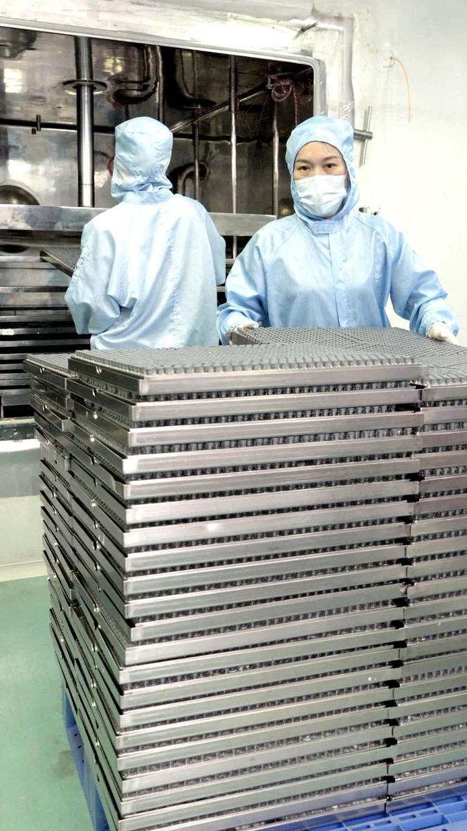 Two operators with stacked vial trays on a production floor